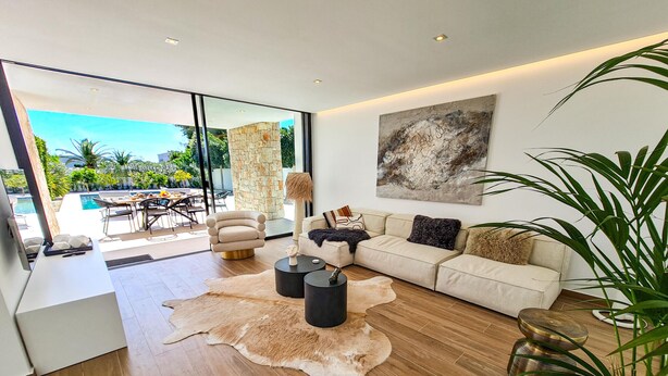 Una sala moderna con sofá, mesa de centro y un gran ventanal con vistas a una piscina y jardín.