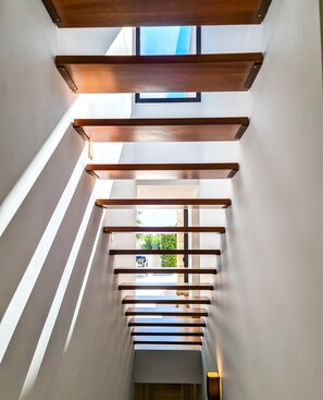 A modern interior with a staircase leading to a lower level, featuring wooden beams and skylights.