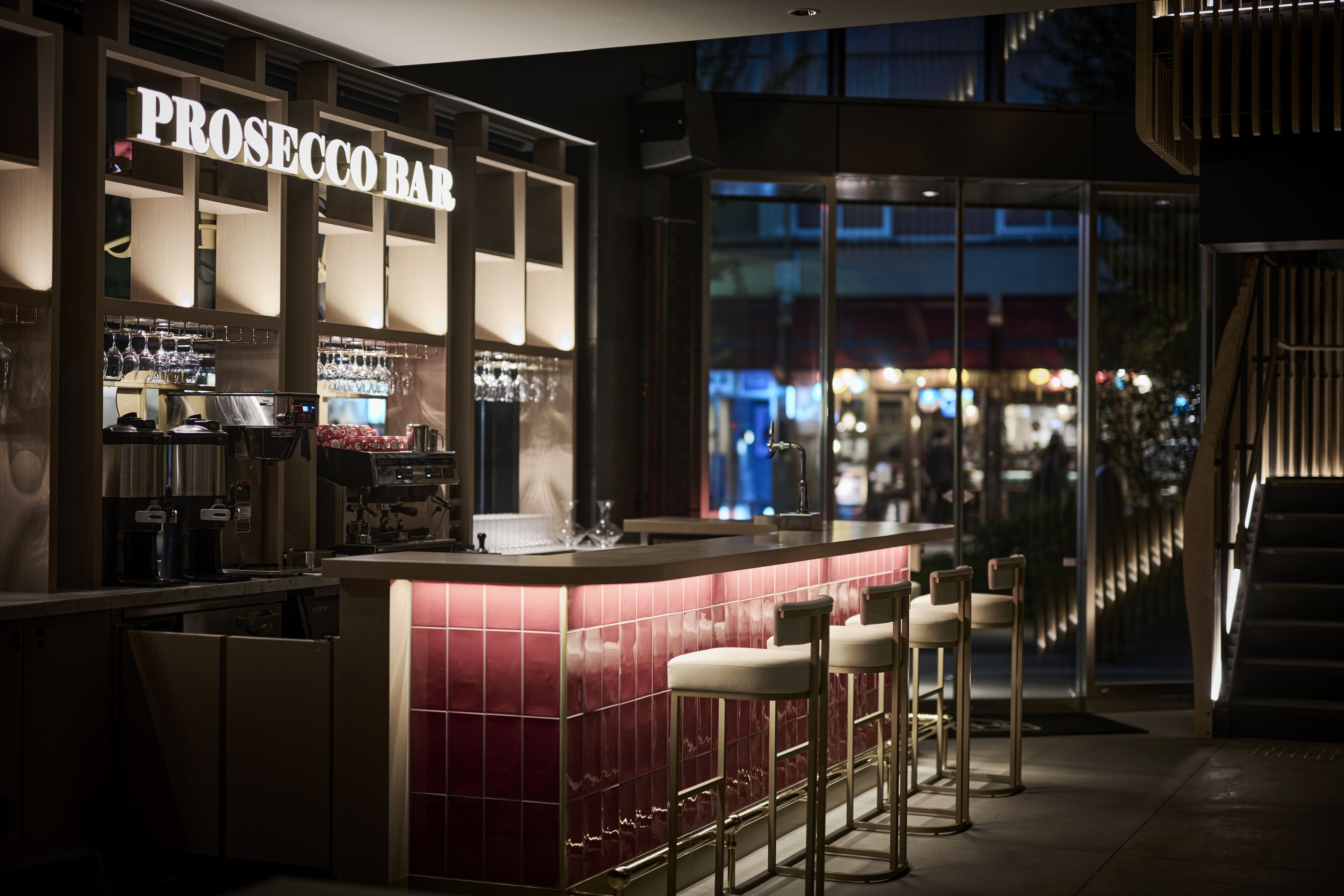 Una zona de bar con mostrador, taburetes y un letrero que dice "PROSECCO BAR".