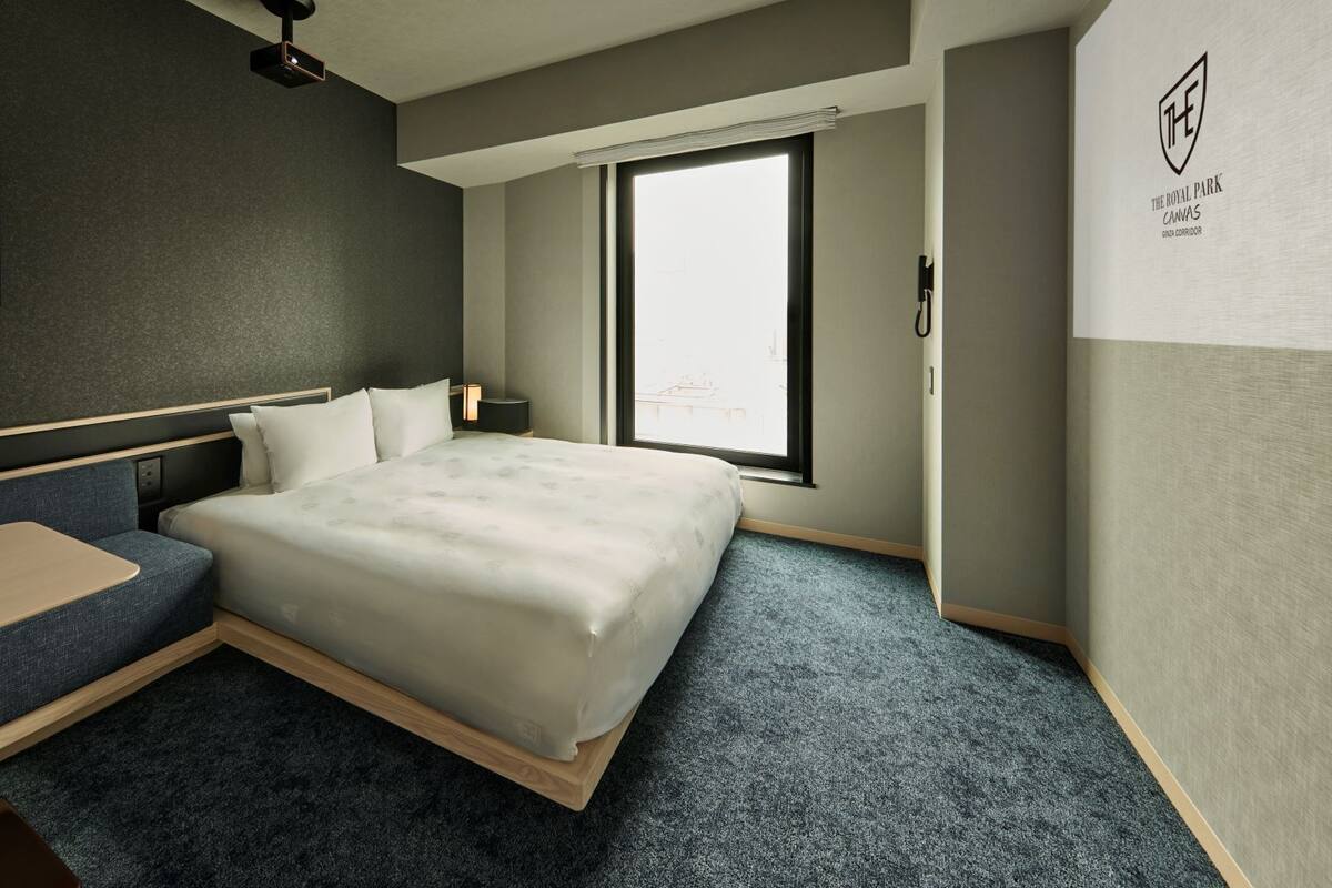 A hotel room with a bed, a desk, a chair, a window, and a wall-mounted artwork.
