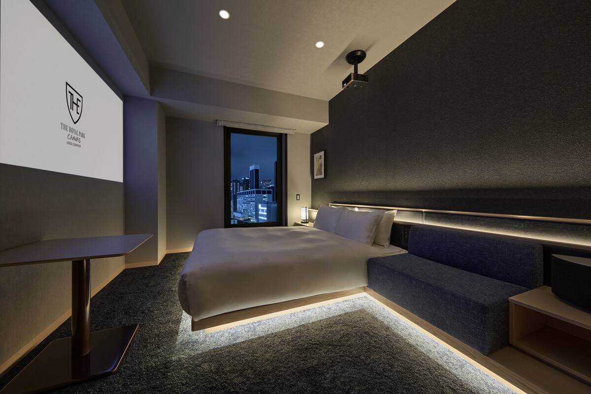 A modern hotel room with a large bed, a desk, and a city view through the window.