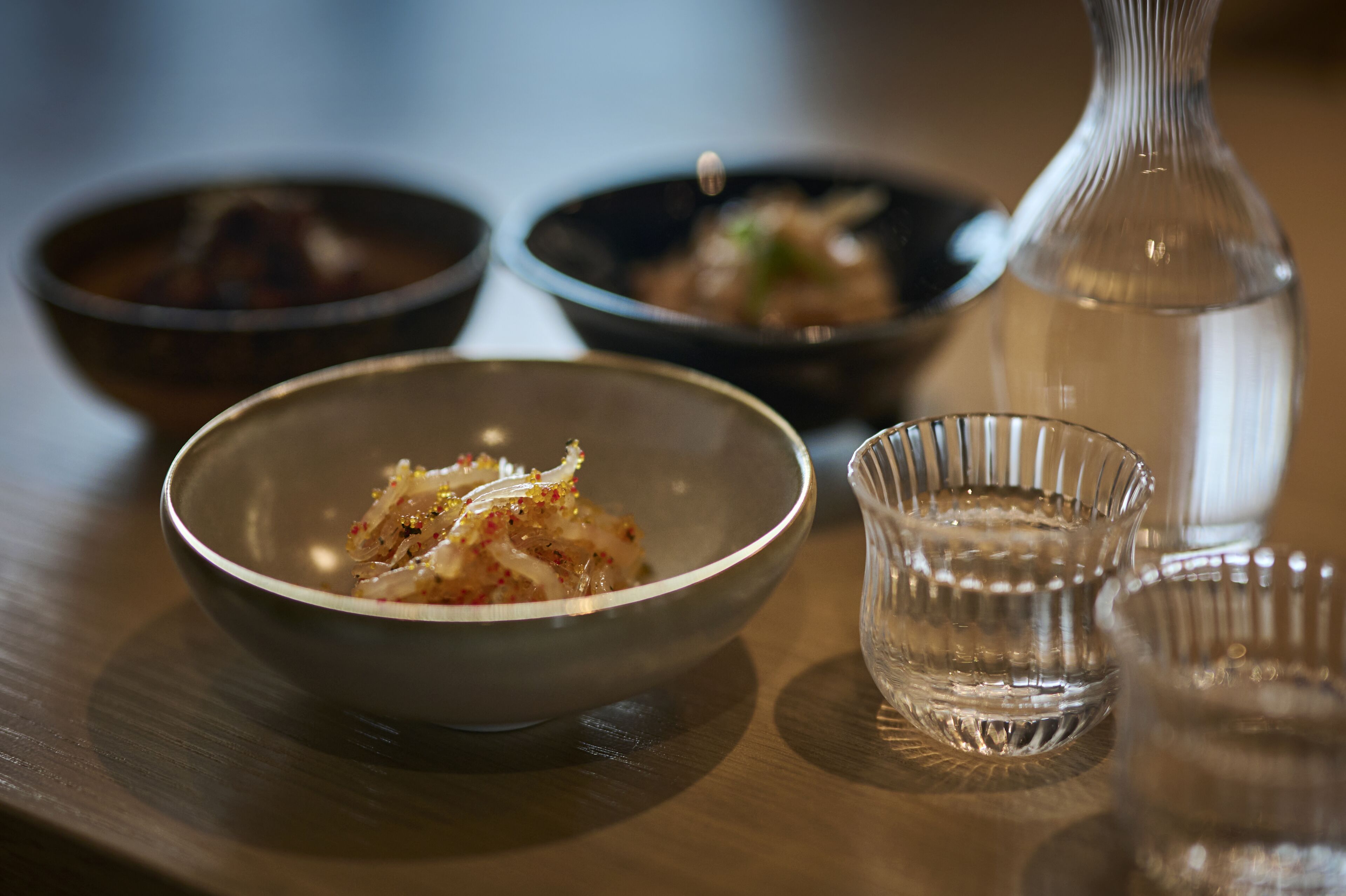 A dining table with three bowls of food and a bottle of water.