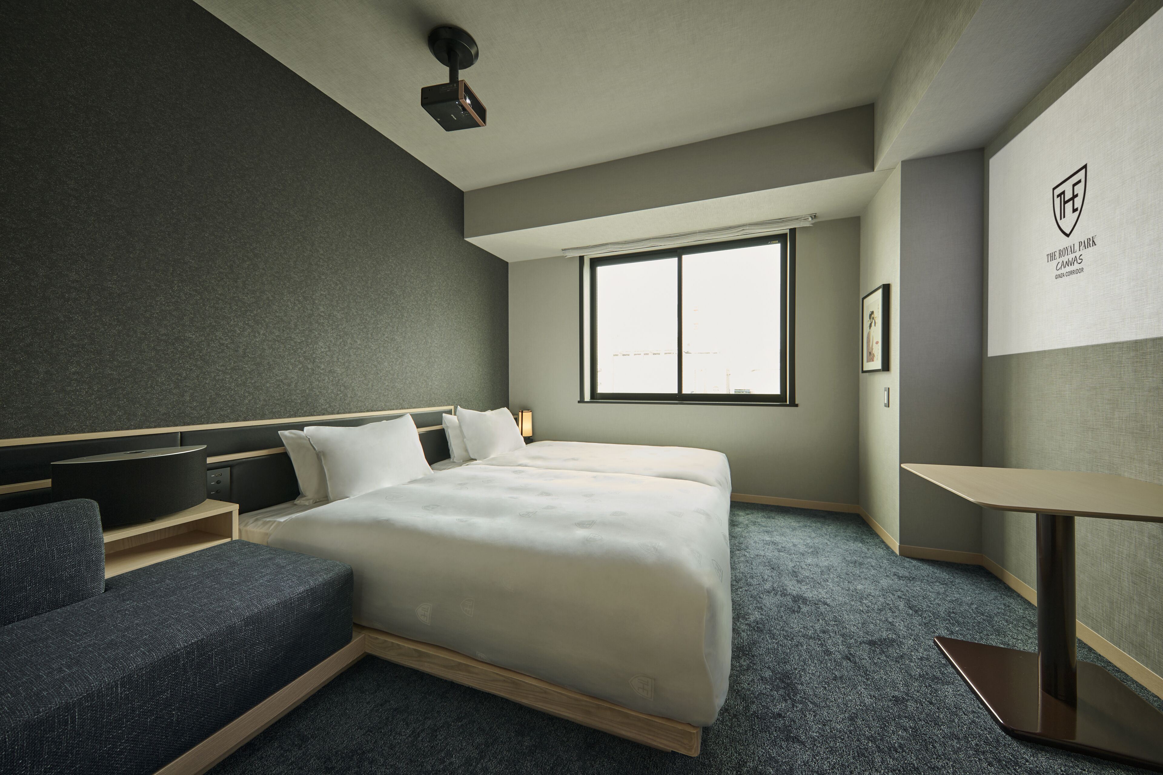 A modern hotel room with a large bed, a seating area, a small table, and a window providing natural light.