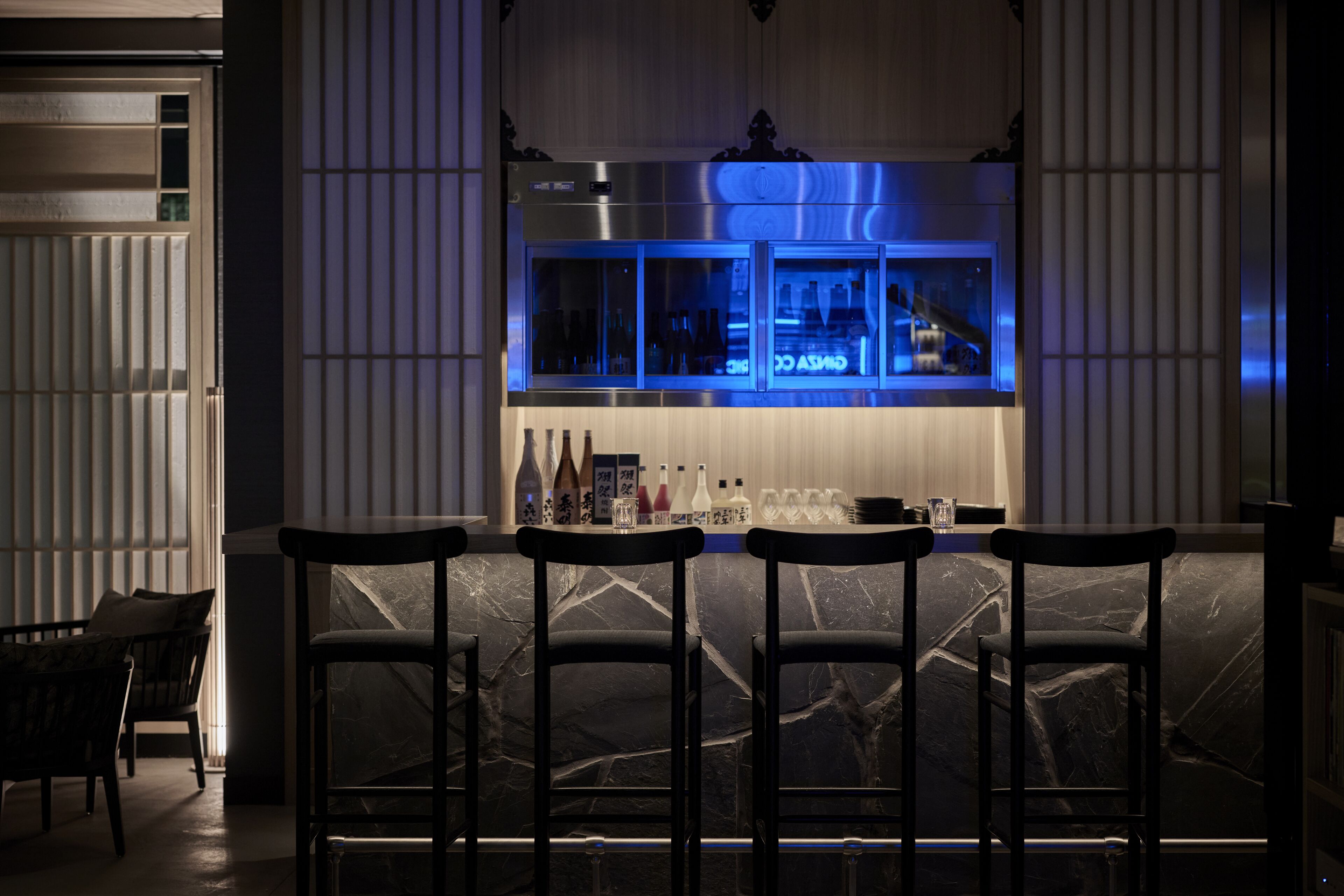 A bar area with a marble countertop, black chairs, and a refrigerated display case with bottles.