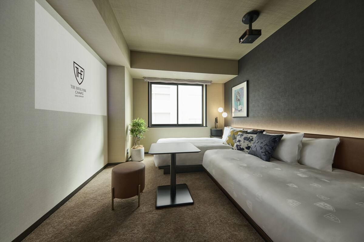 A modern hotel room with a bed, a small table, a potted plant, and a wall-mounted artwork.