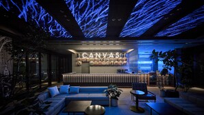 A modern lounge area with a sofa, coffee table, and chairs, featuring a neon sign for 'CANVAS' and a neon sign for 'LA CORRIDOR'.