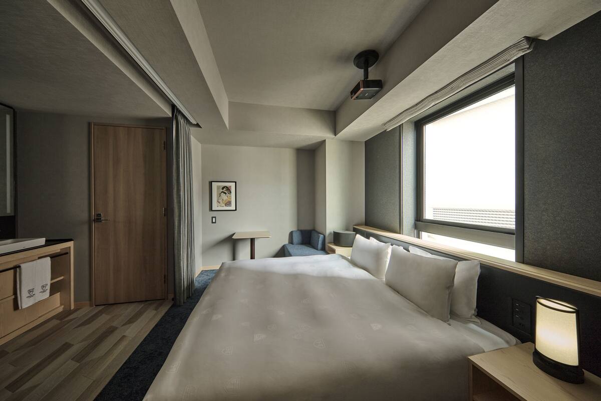 A hotel room with a large bed, a desk, a chair, a window with blinds, and a wall-mounted TV.