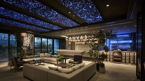 A modern lounge area with a sofa, armchairs, and a coffee table. A neon sign reads "CANVAS" and "GINZA CORRIDOR".
