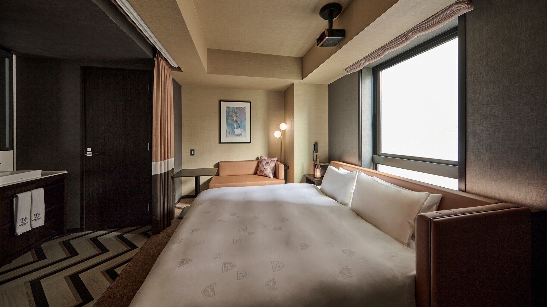 Een hotelkamer met een bed, een bank, een bureau en een groot raam.