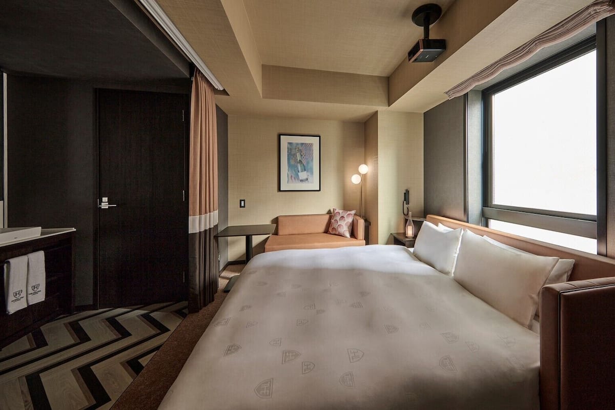 Una habitación de hotel con cama, sofá, escritorio y un amplio ventanal.