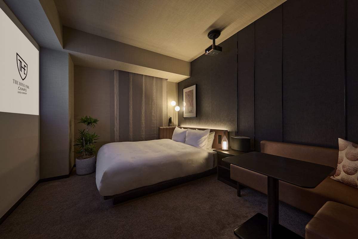 Moderni hotellihuone, jossa on suuri sänky, yöpöytä lampun kanssa, pieni pöytä ja sohva.