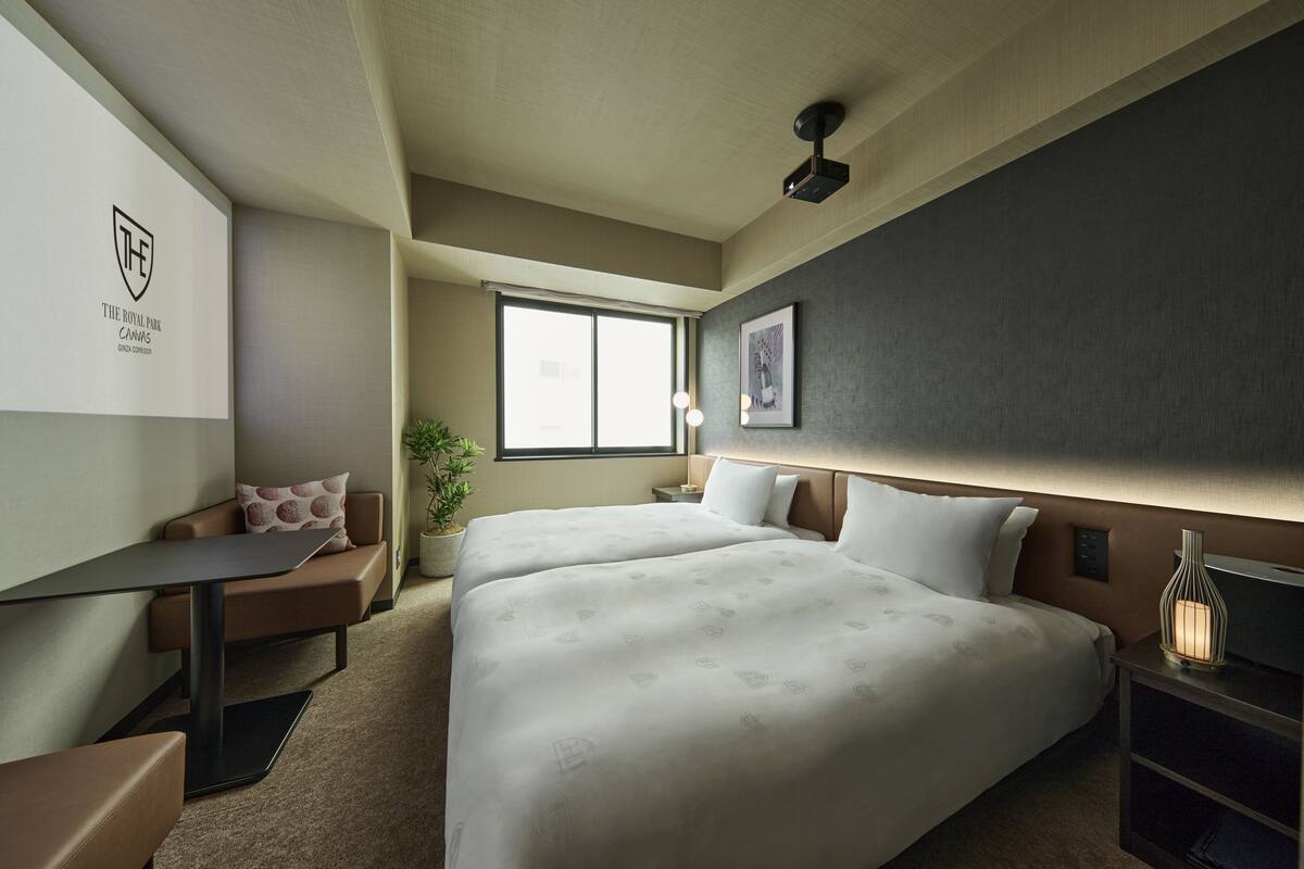 A hotel room with a bed, a desk, a chair, a nightstand, and a window.