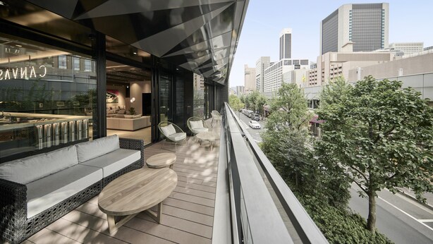 A modern outdoor seating area with a sofa and tables, overlooking a cityscape.