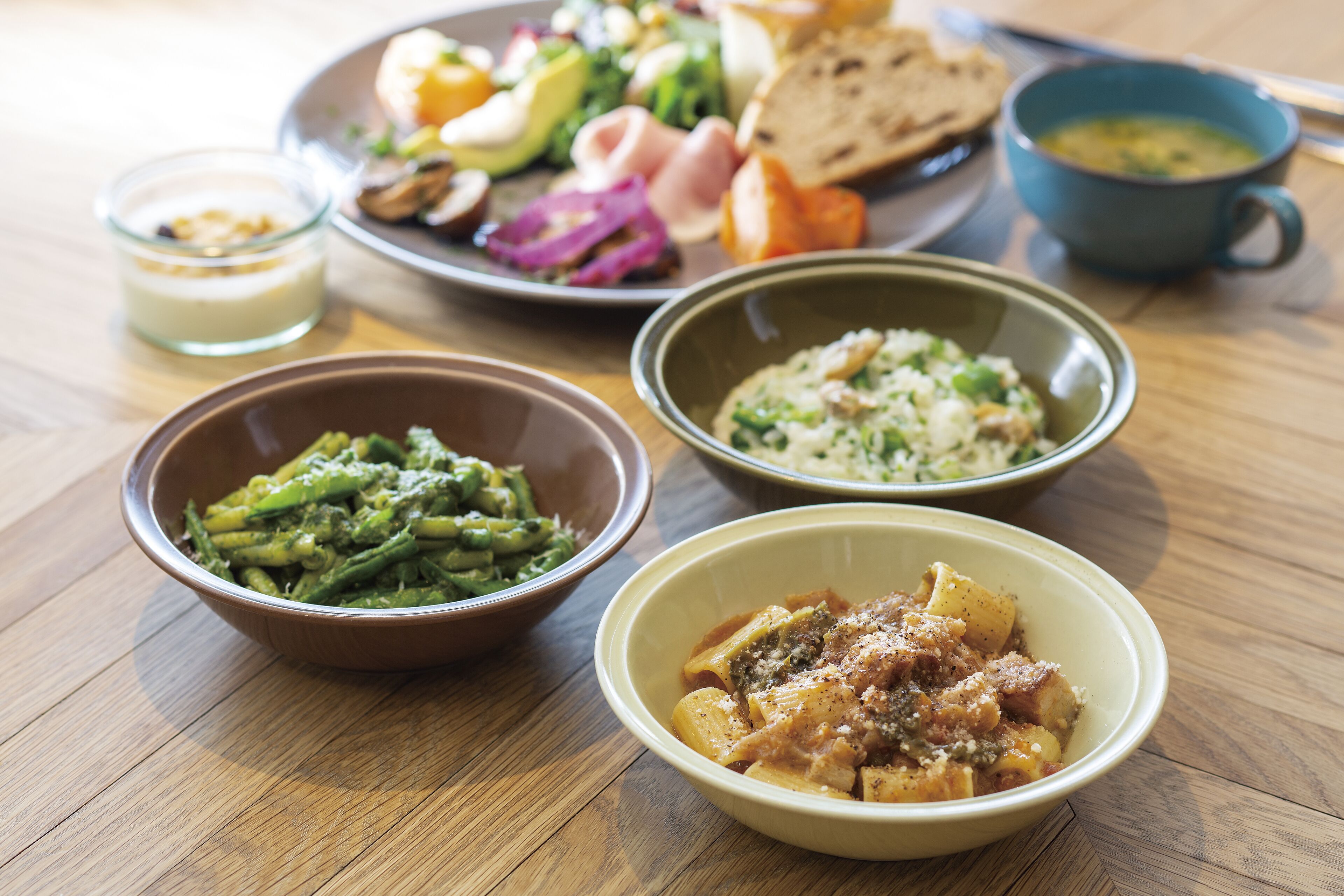 Una mesa de madera con varios platos, incluyendo pasta, judías verdes y sopa.