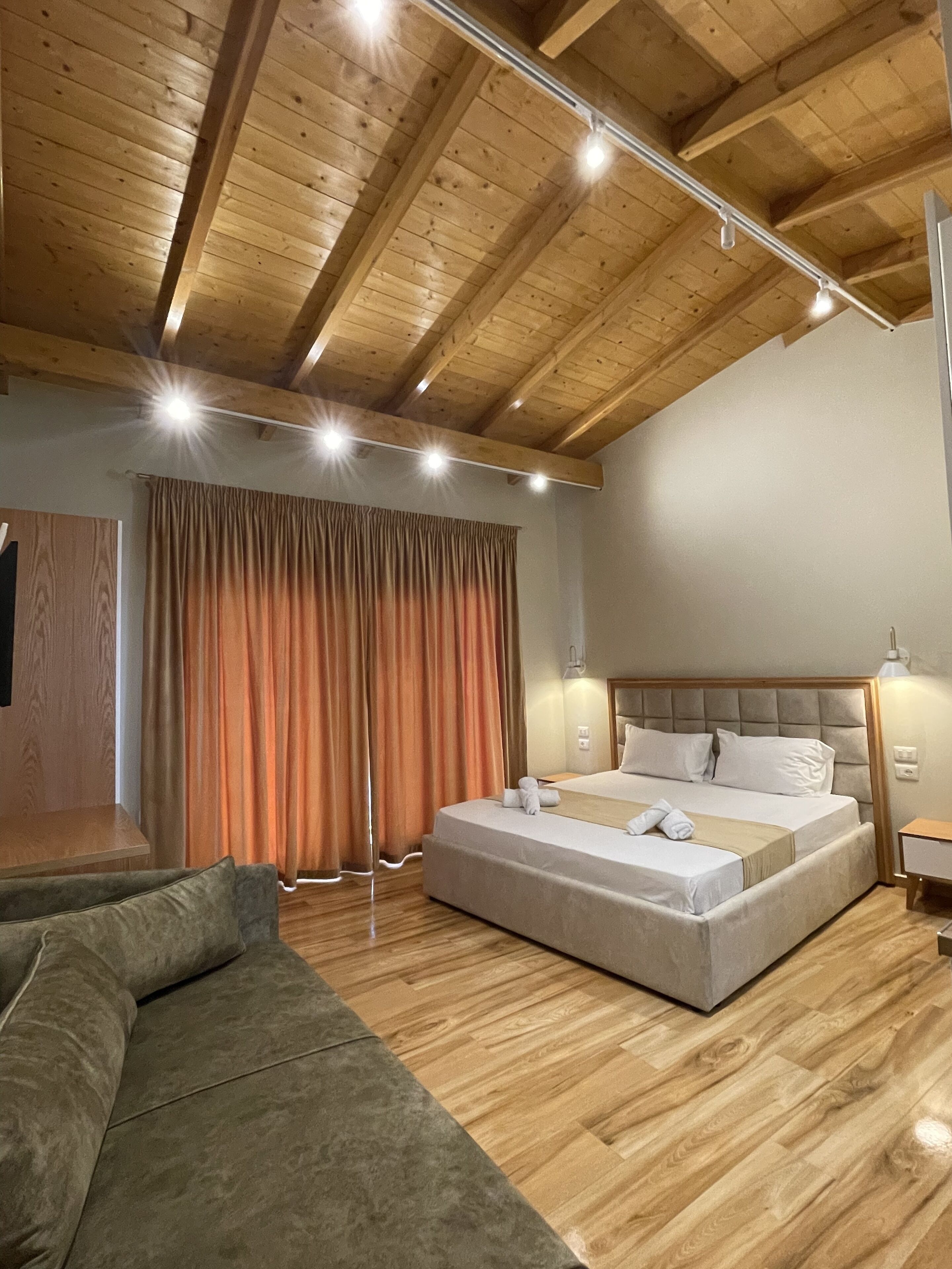 A modern bedroom with a large bed, a sofa, wooden flooring, and a sloped ceiling with exposed beams.