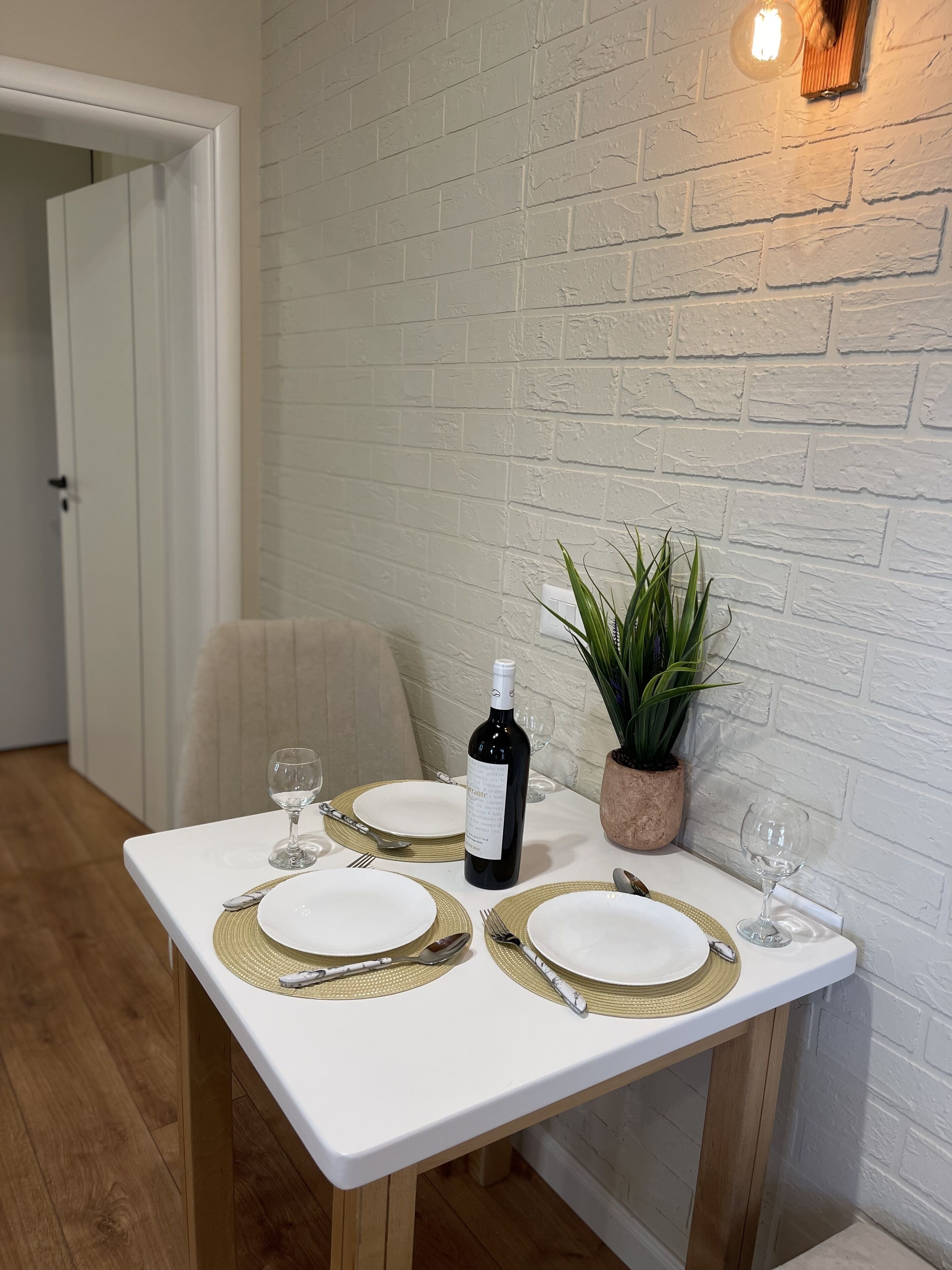 A dining table set with white plates, gold placemats, and a bottle of wine.