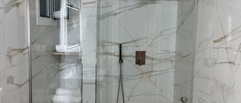 A modern bathroom with a glass-enclosed shower, marble walls, and wooden flooring.