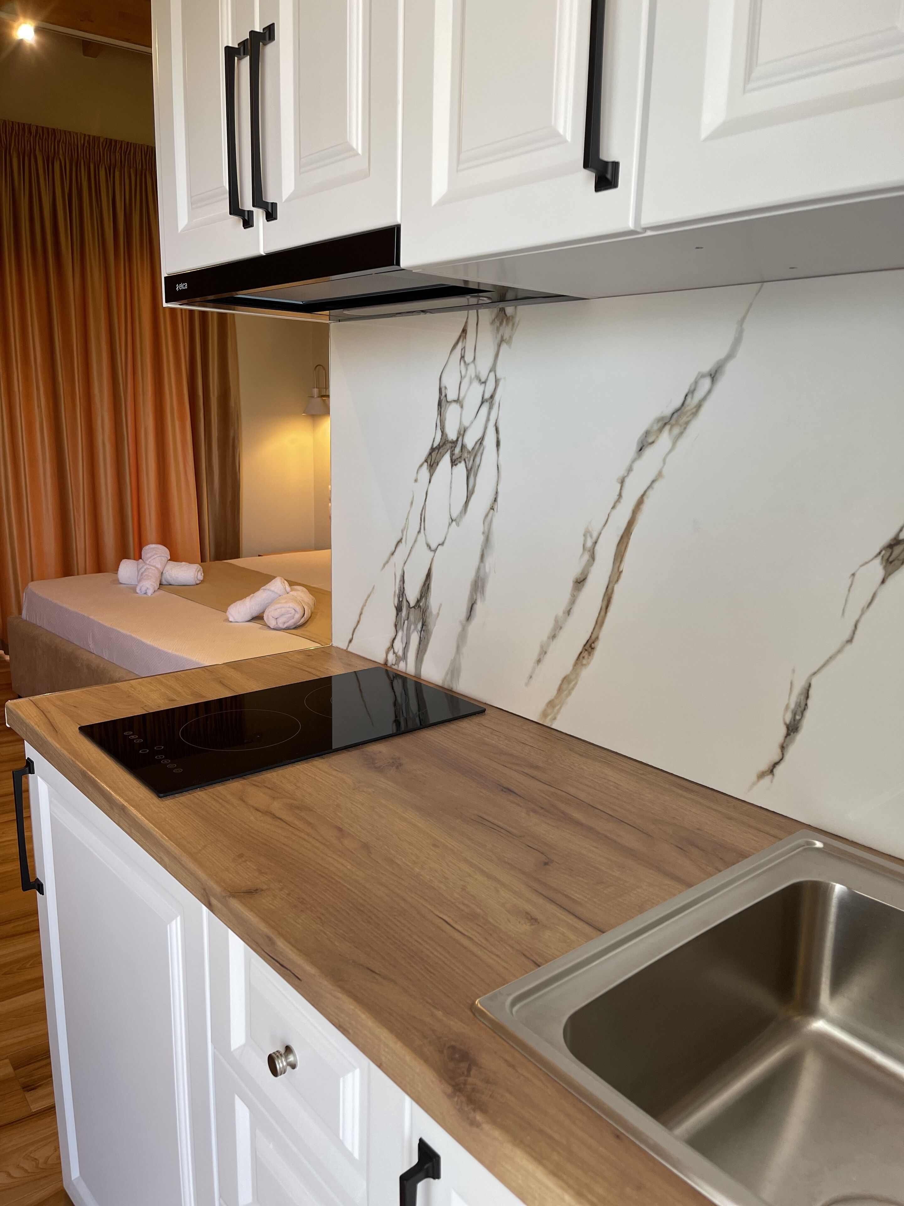 A modern kitchen with white cabinets, a marble backsplash, a black induction cooktop, and a stainless steel sink.