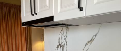 A modern kitchen with white cabinets, a marble backsplash, a black induction cooktop, and a stainless steel sink.