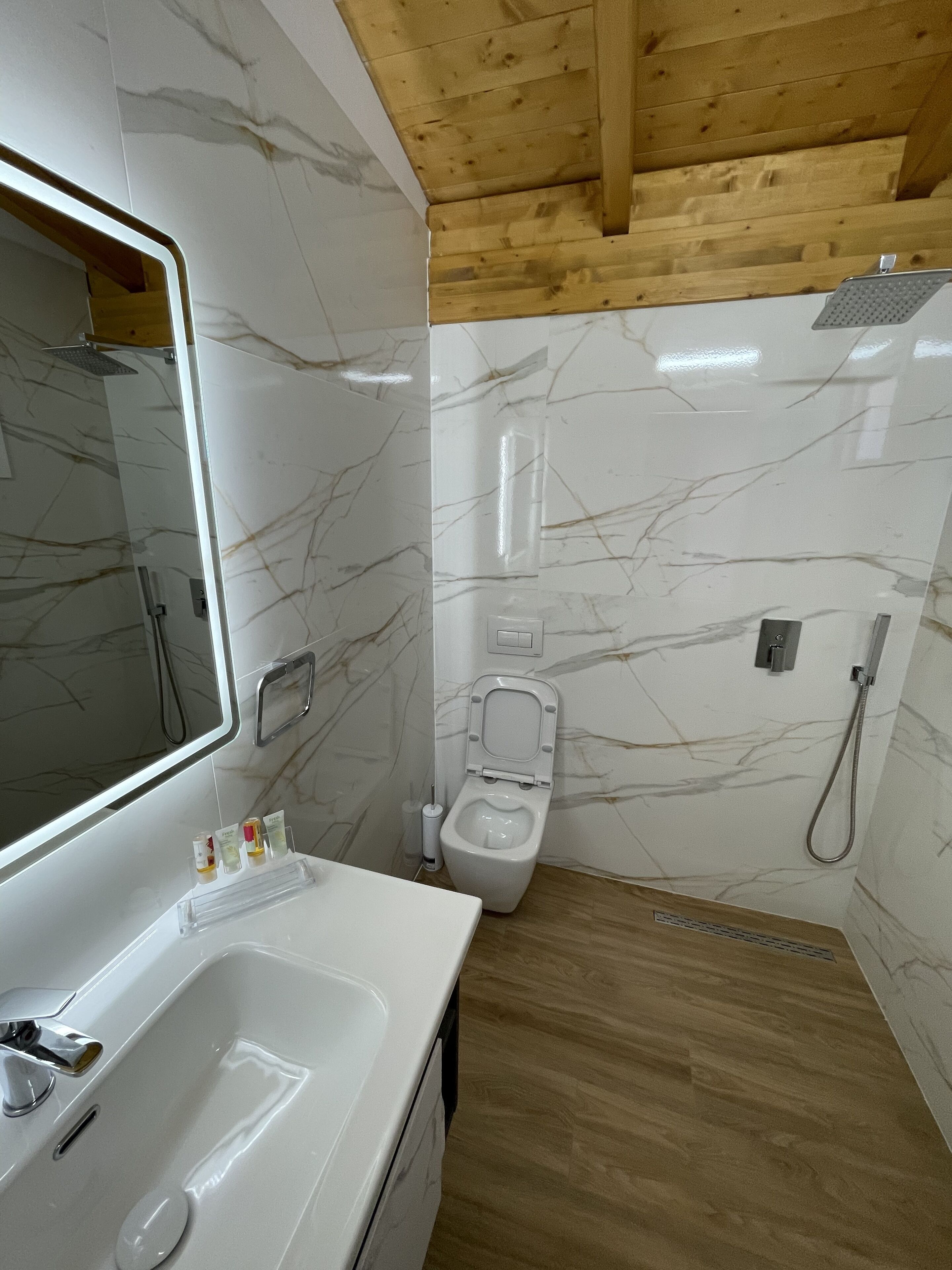 A bathroom with a marble wall, a wooden ceiling, a sink, a toilet, and a shower.