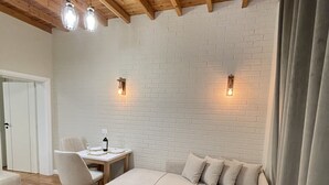 Ein gemütliches Zimmer mit Holzboden, einer weißen Ziegelwand, einer Couch, einem Esstisch mit Stühlen und Pendelleuchten.