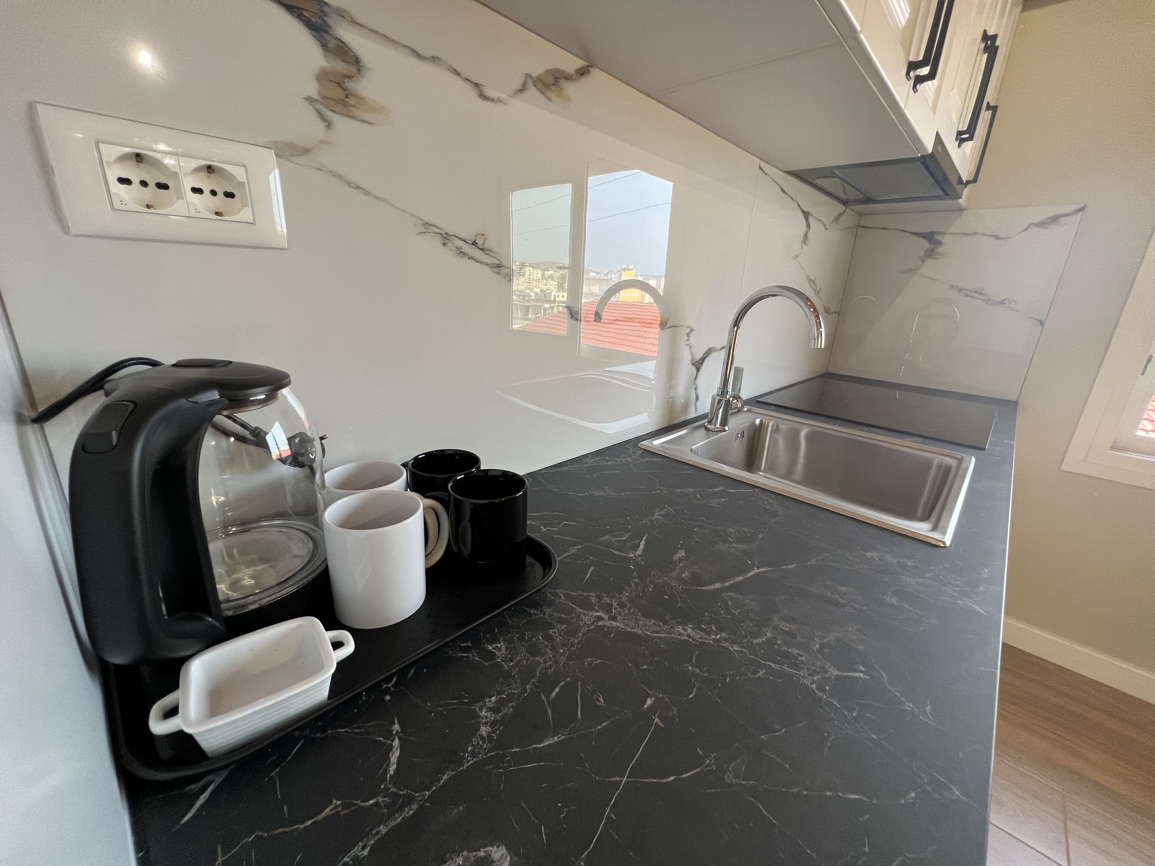 Une cuisine moderne dotée d’un plan de travail en marbre noir, d’une machine à café intégrée, d’un évier et d’une fenêtre offrant une vue sur l’extérieur.