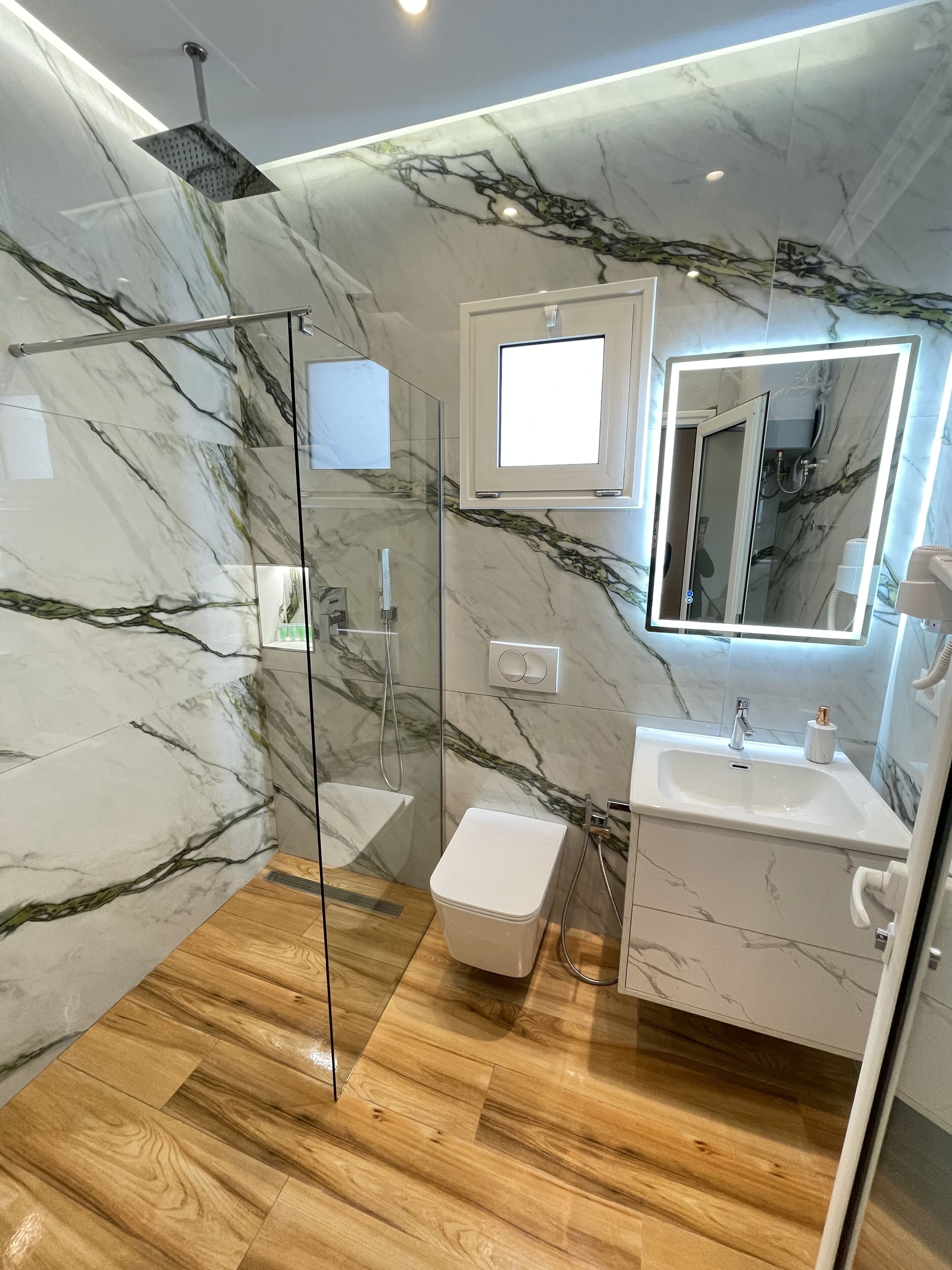 A modern bathroom with a glass-enclosed shower, a marble wall, a sink, and a toilet.