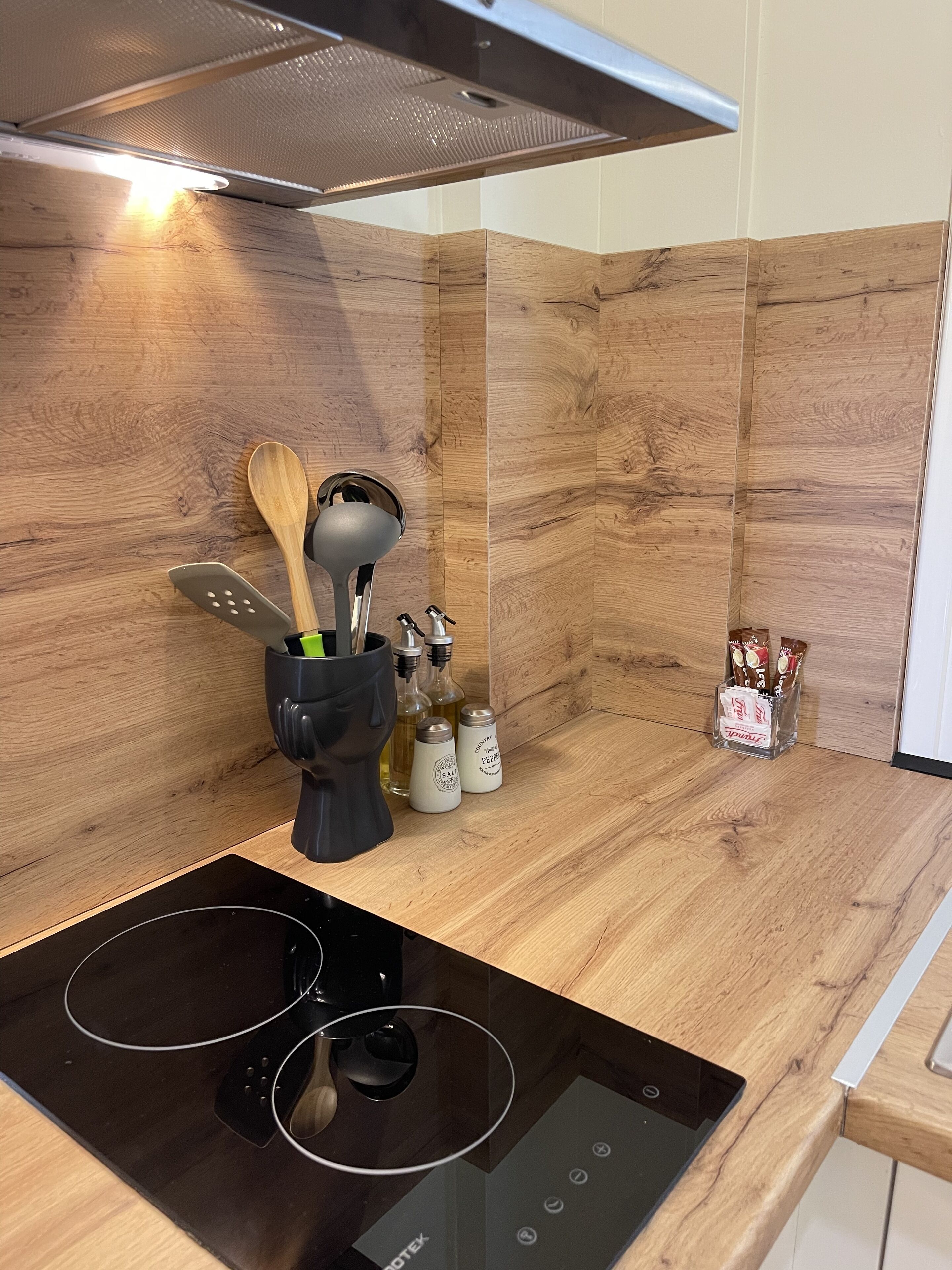 A modern kitchen with a built-in stove, wooden backsplash, and various kitchen utensils and appliances.