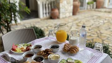 An outdoor dining table set with a variety of foods and drinks, surrounded by stone walls and potted plants.