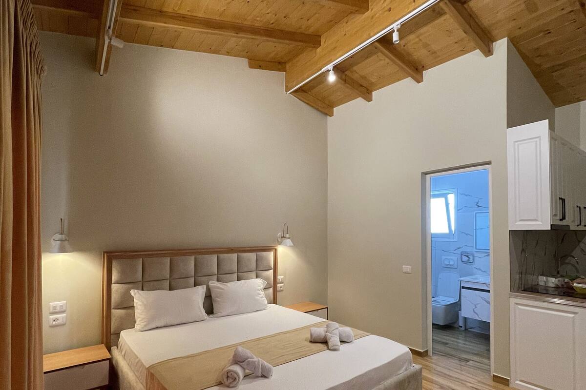 Ein Schlafzimmer mit Holzboden, einem Bett mit Kopfteil, einem Nachttisch und einem durch eine offene Tür einsehbarer Badezimmer.