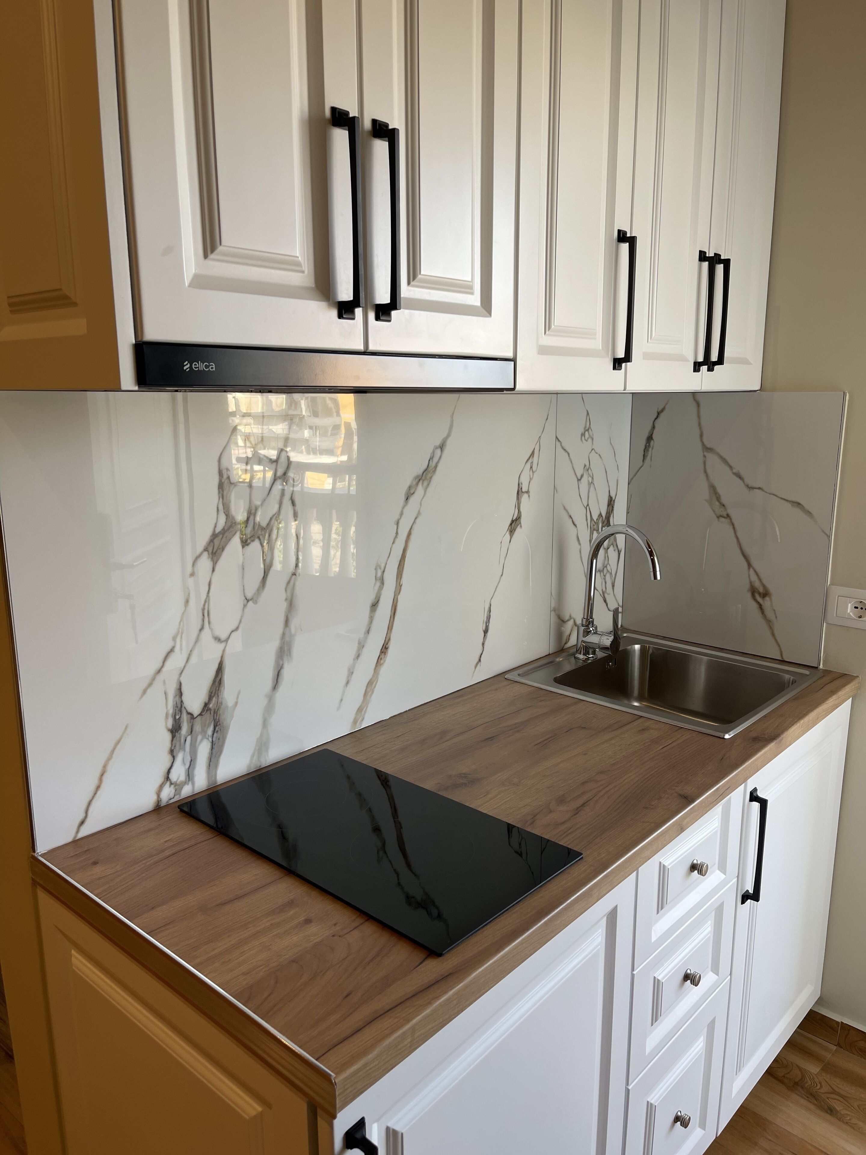 Een keuken met witte kastjes, zwarte handgrepen, een zwart aanrecht en een marmeren achterwand.