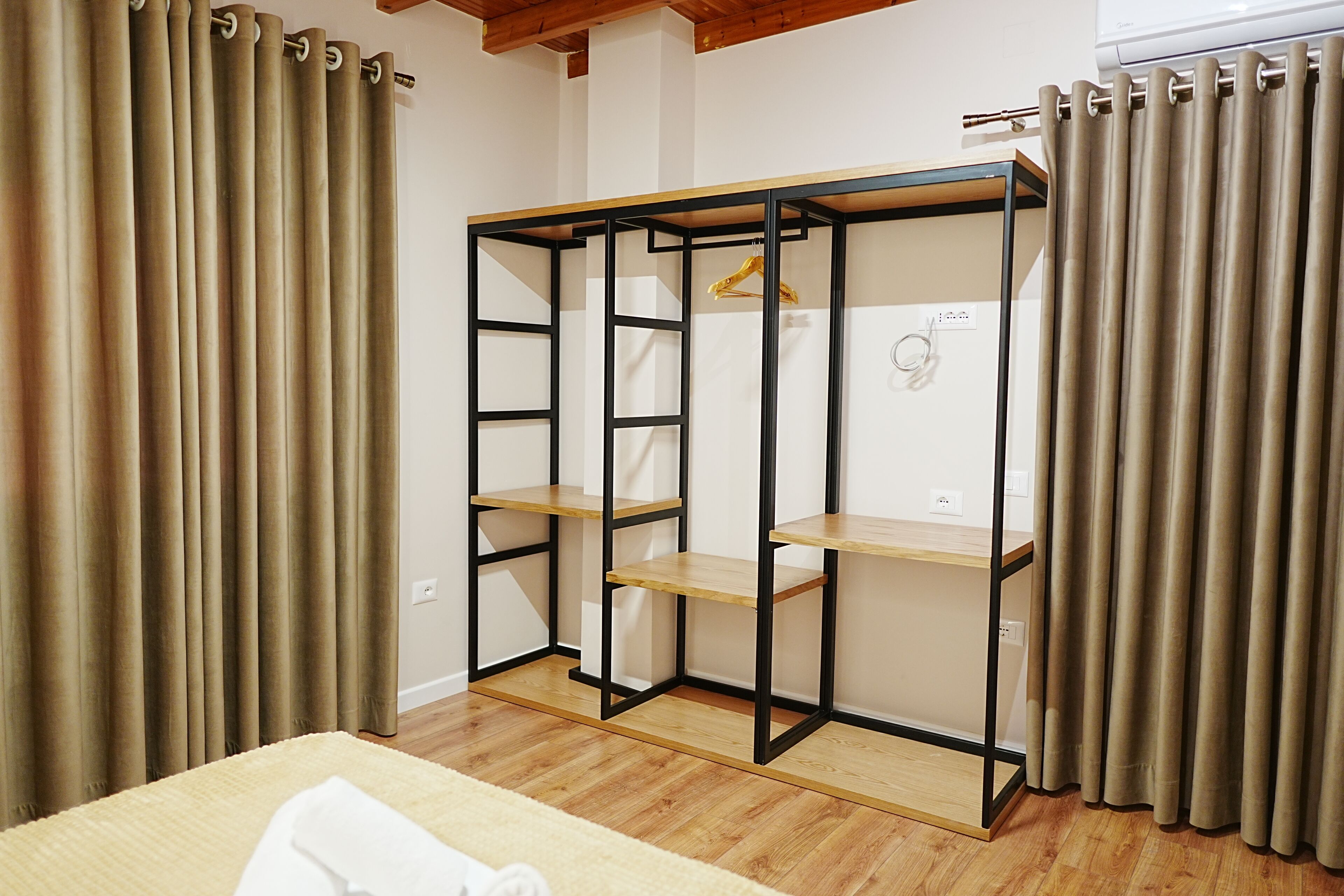 A bedroom with a bed, a wardrobe with shelves, and a hanging rack.