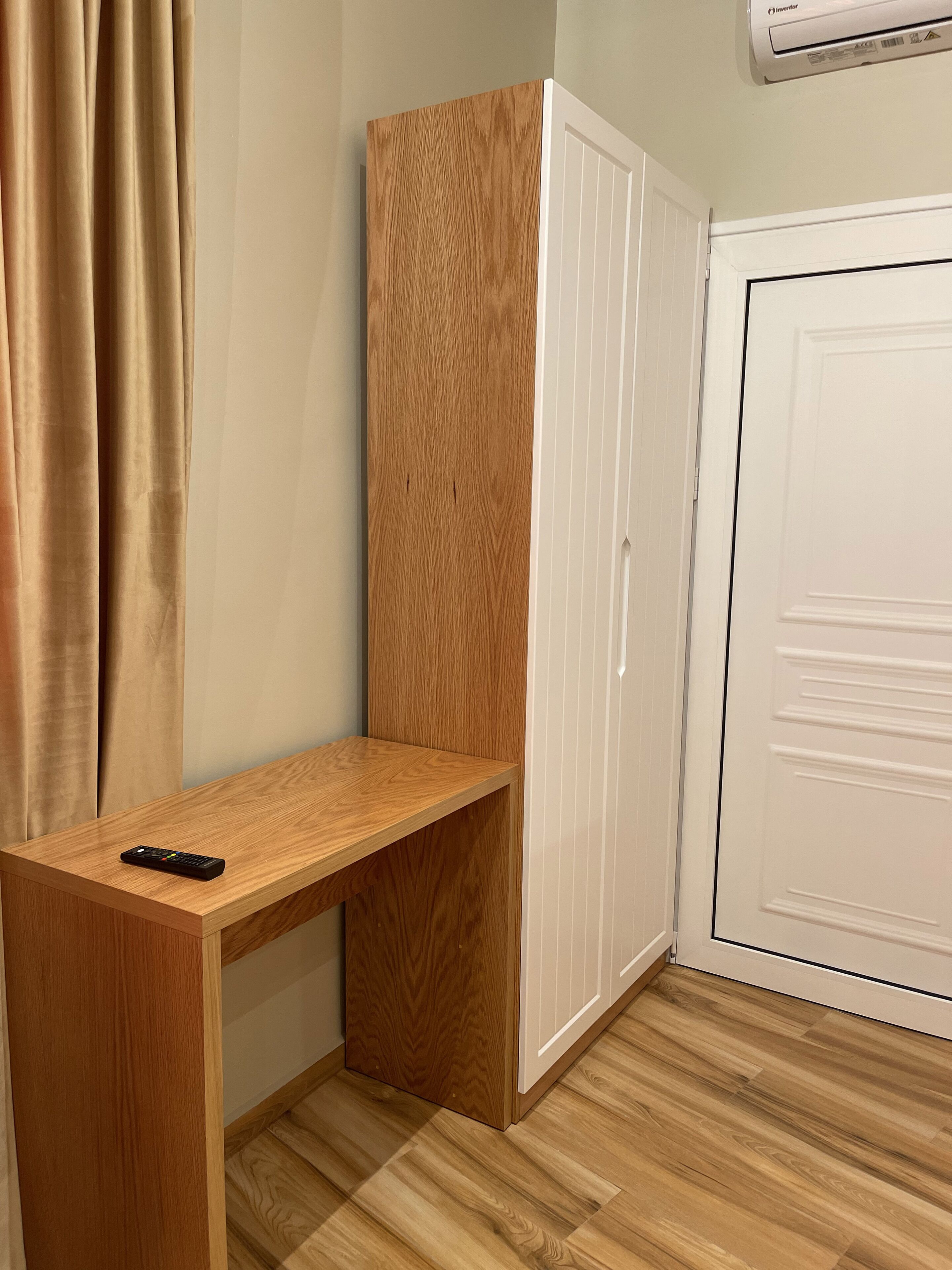 A room with a wooden desk, a wardrobe, and a white door.