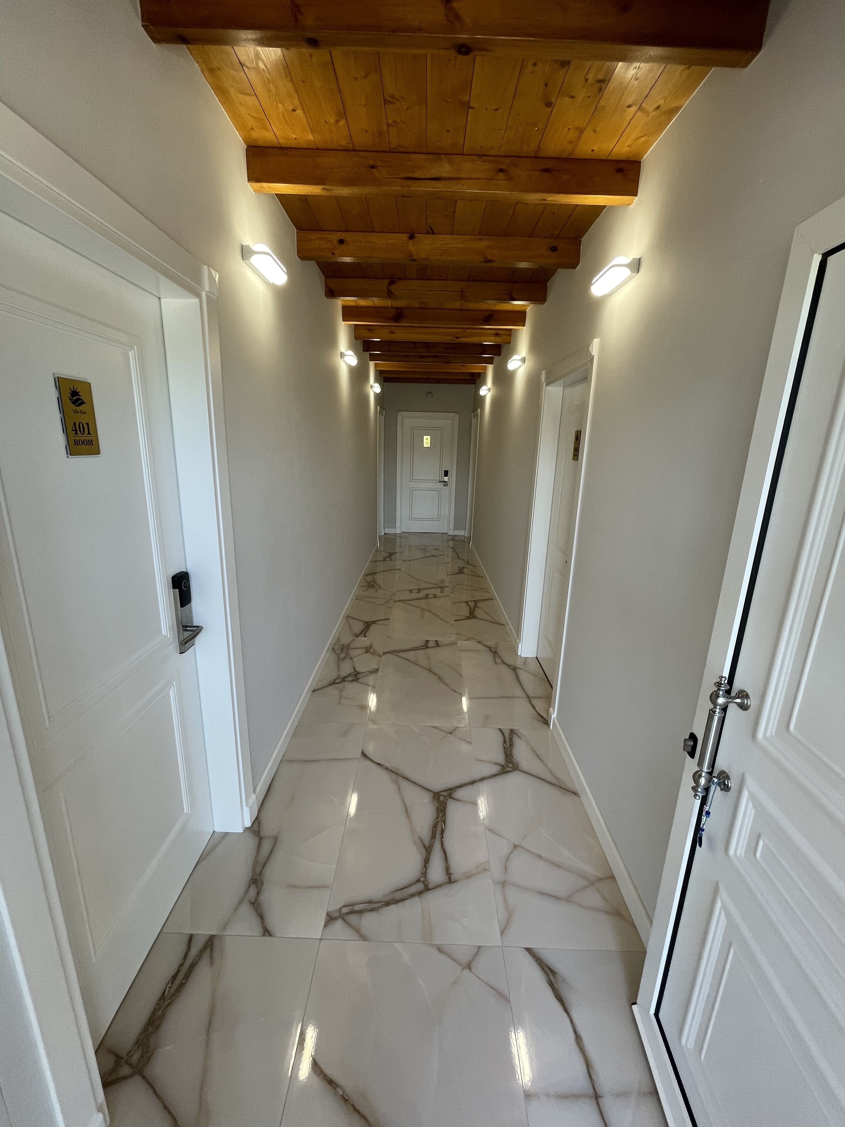 A hallway with white walls, a marble floor, and wooden ceiling beams. There are doors on both sides, one of which has a sign indicating room number 401.