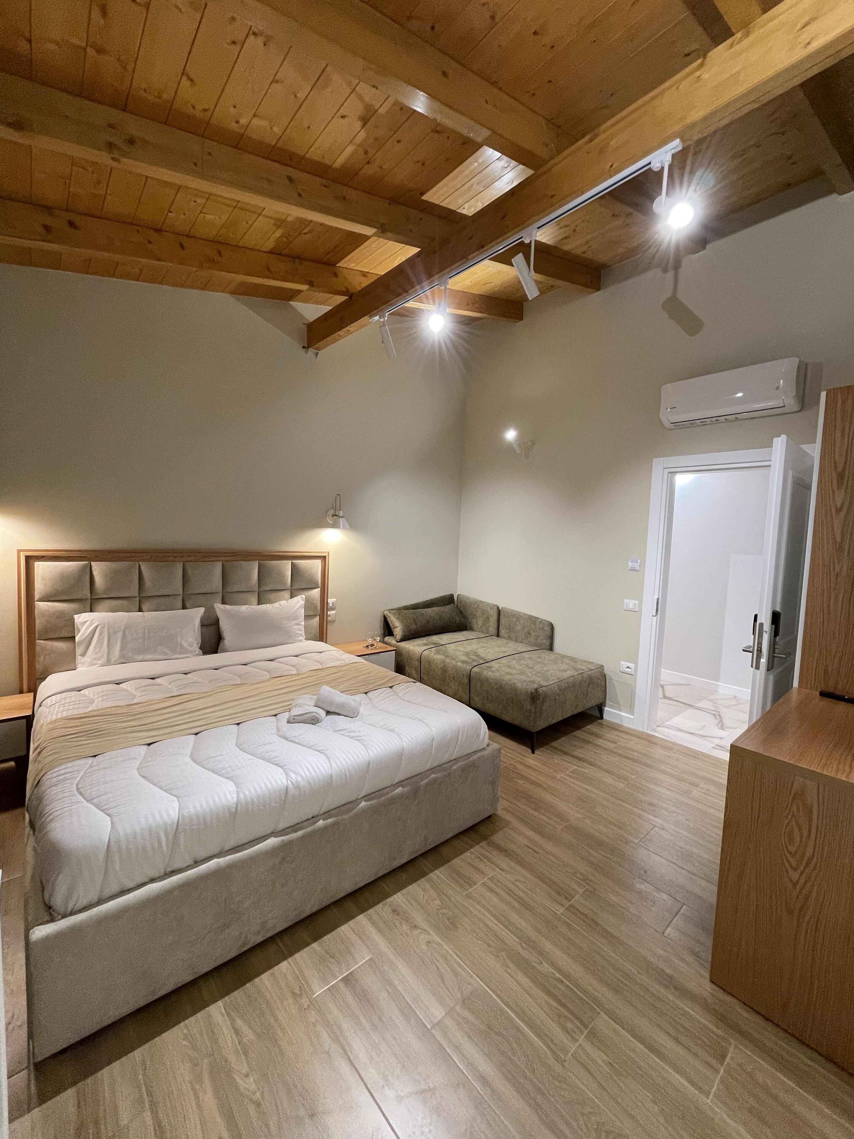 A bedroom with a large bed, a sofa, a wooden ceiling, and a door.