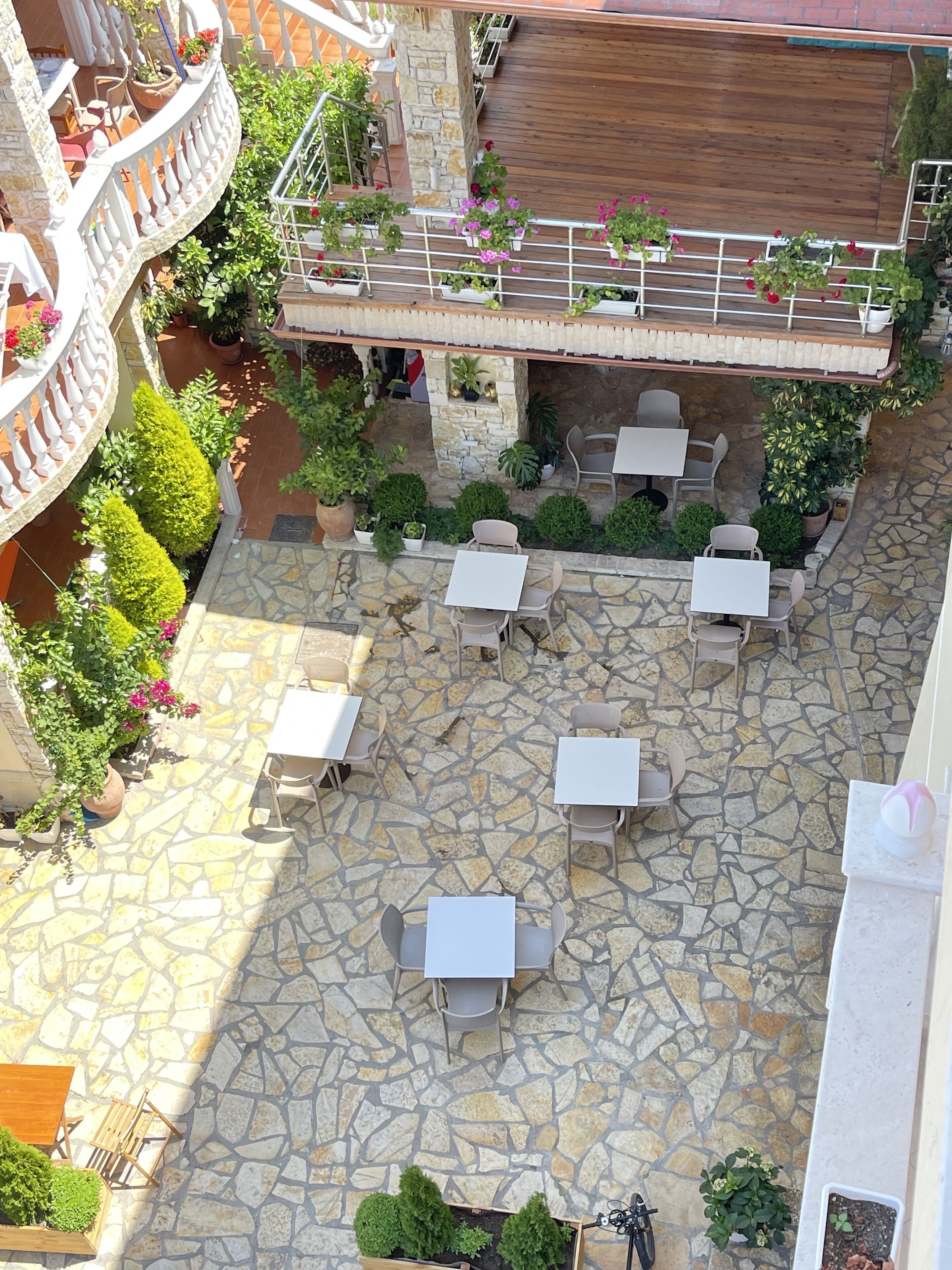 An outdoor patio with stone flooring, white tables, and potted plants.
