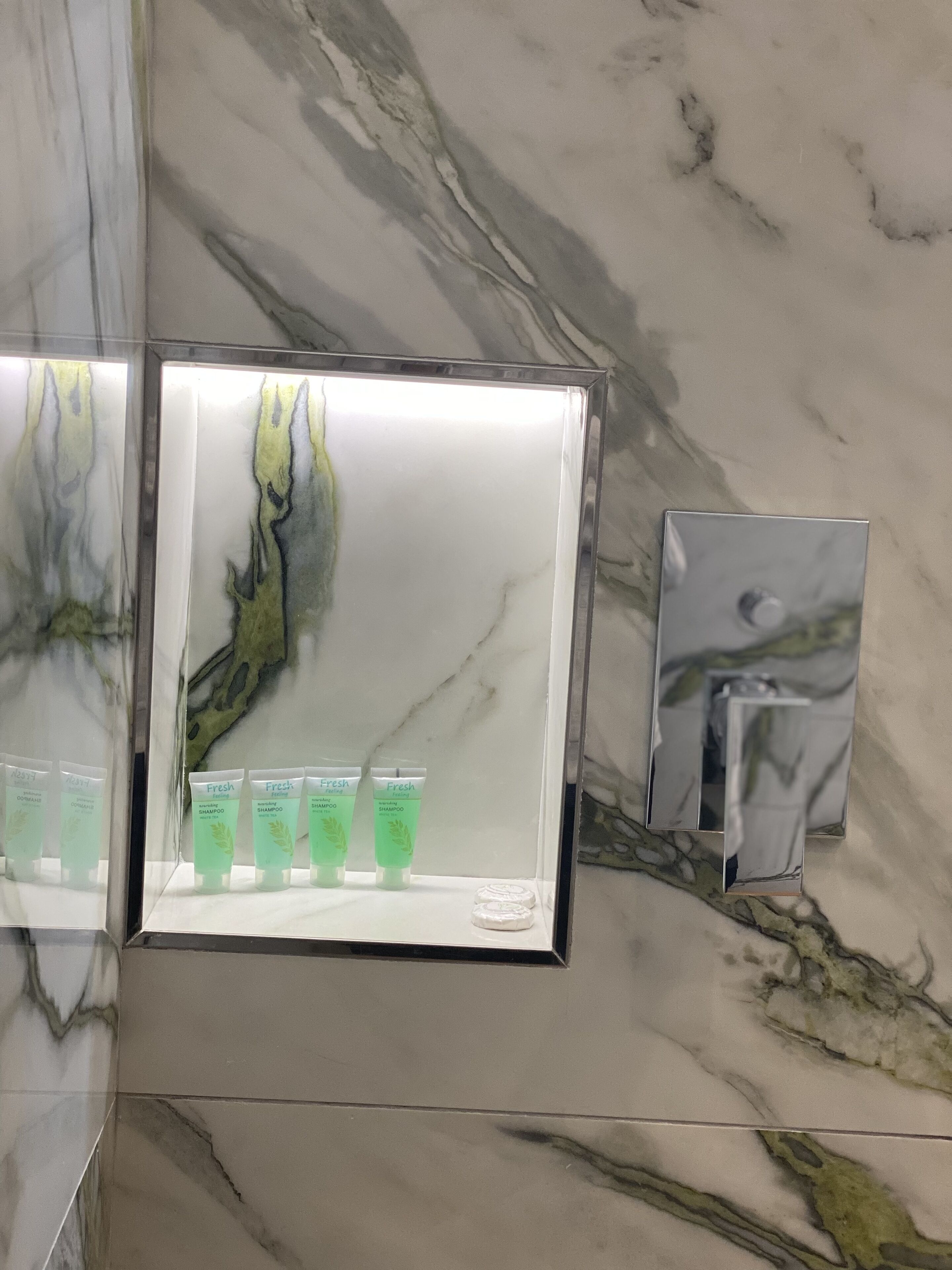 Un bagno con una parete in marmo e uno scaffale con bottiglie di shampoo.