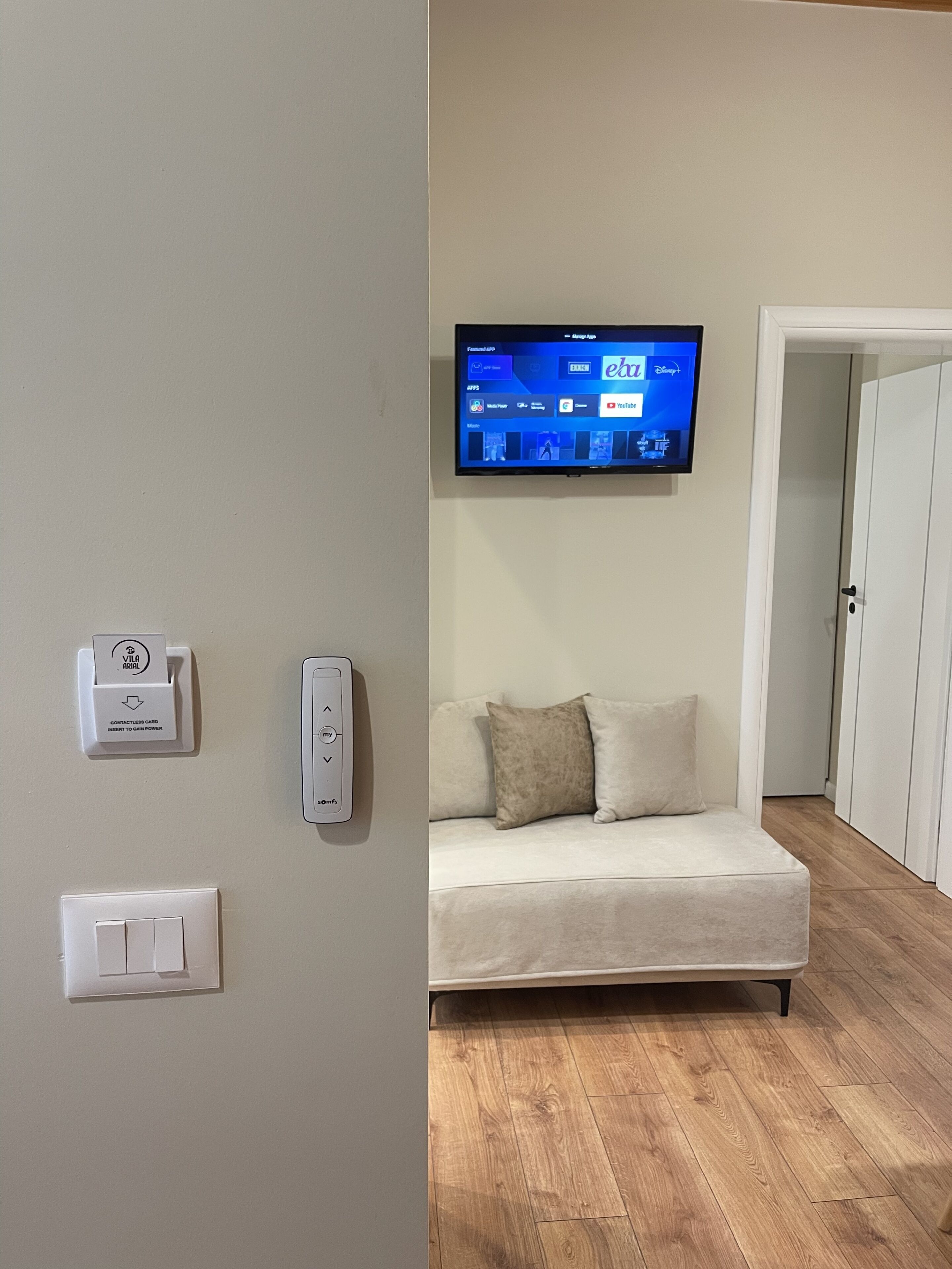 Ein modernes Wohnzimmer mit einem an der Wand befestigten Flachbildfernseher, einem berührungslosen Kartenlesegerät, einem intelligenten Thermostat und einem Lichtschalter.