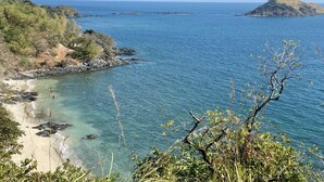 A coastal landscape with clear blue waters, rocky shores, and a sandy beach.