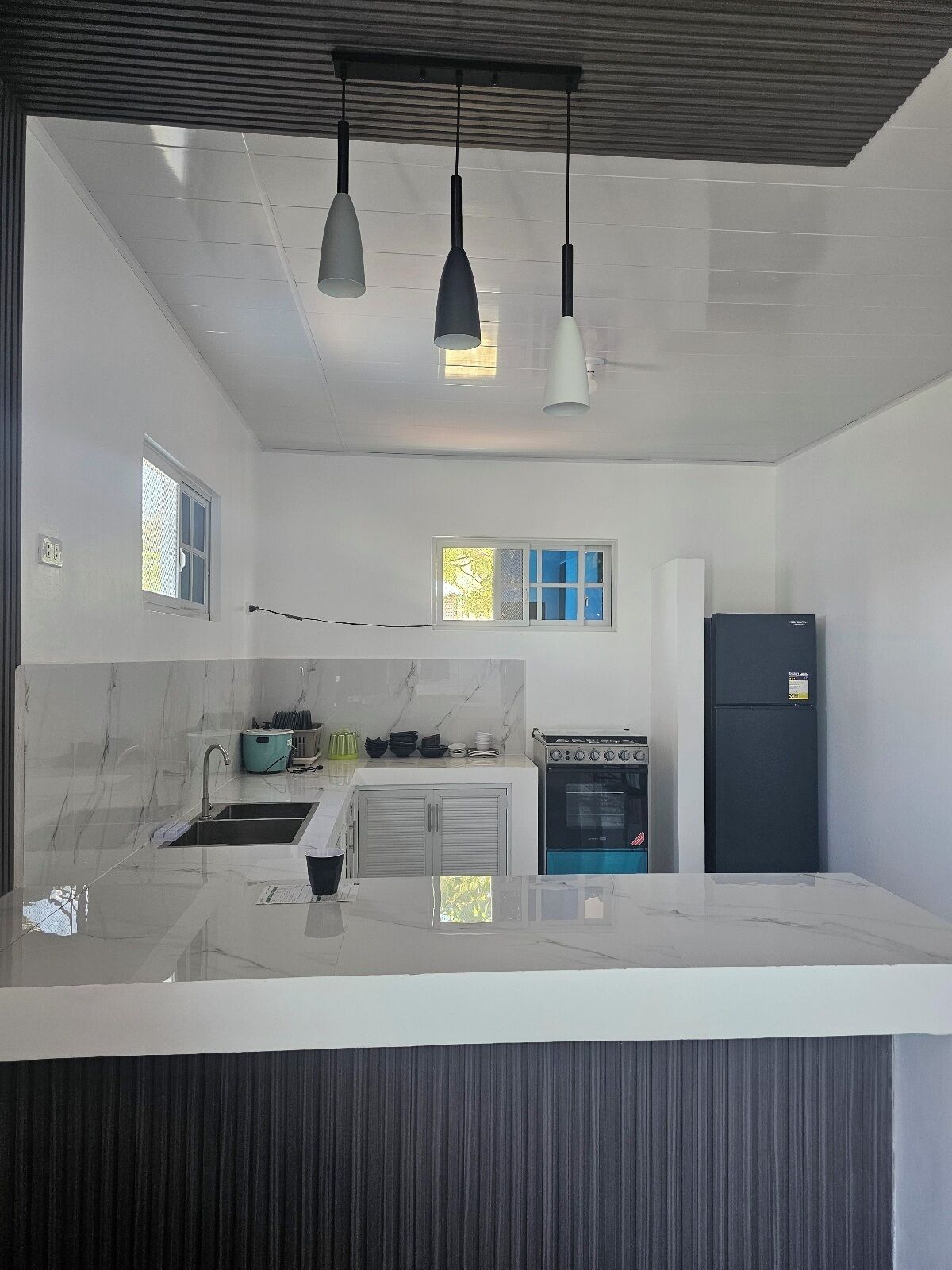 Una cocina moderna con encimera de mármol, estufa, refrigerador y luces colgantes.