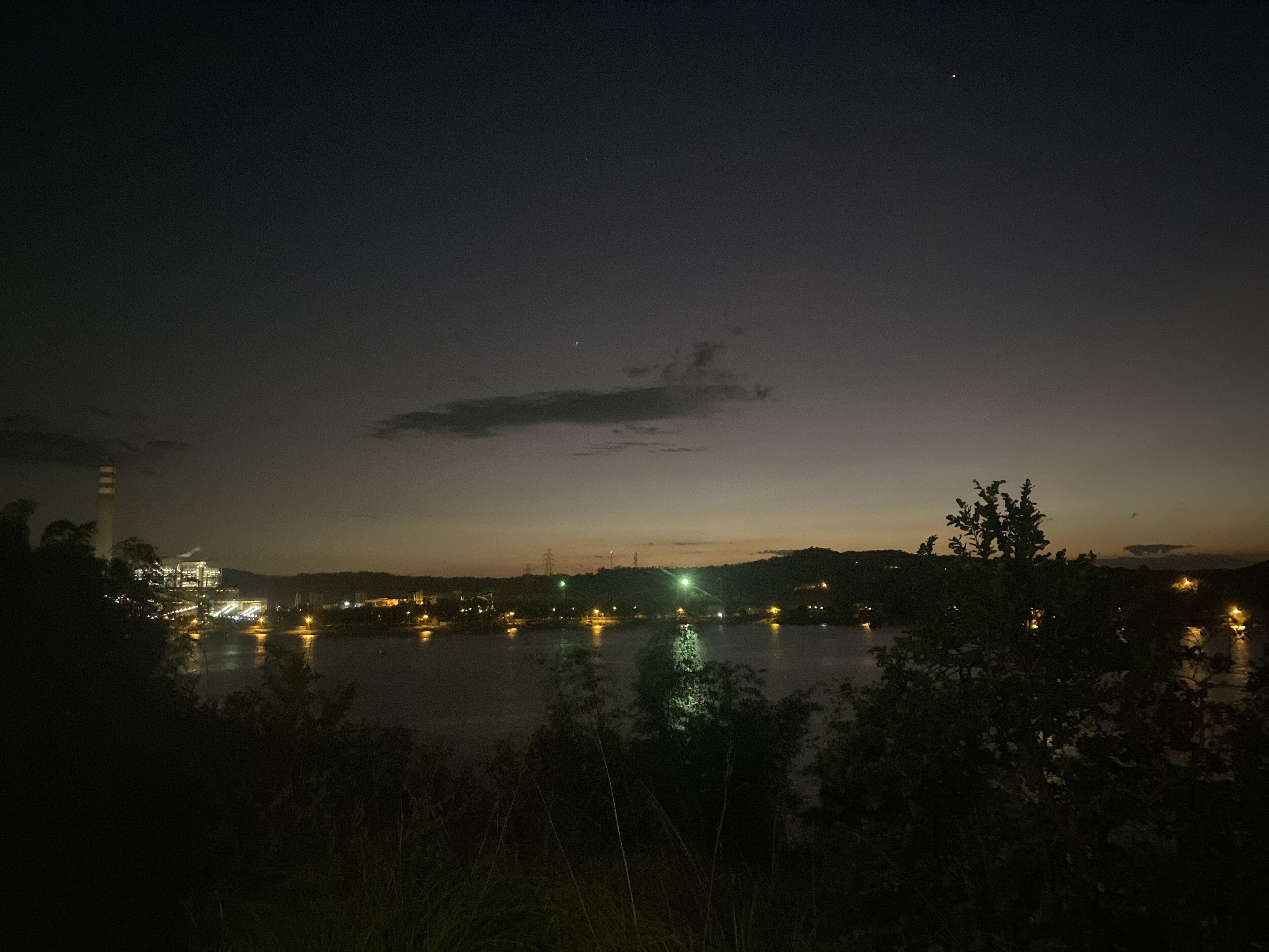 Une vue nocturne d’une zone riveraine, avec des bâtiments et des lumières qui se reflètent sur l’eau.