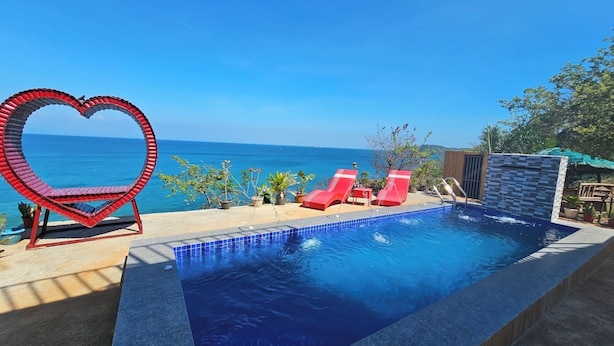 A swimming pool with a heart-shaped structure, red lounge chairs, and a view of the sea.
