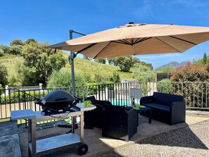 An outdoor patio with a grill, dining table, and outdoor furniture under a large umbrella. - 10 min from the beaches of saint florent: house with private pool and garden (Oletta)