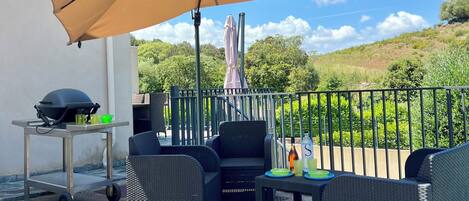 An outdoor patio with wicker furniture, a grill, and a large umbrella.