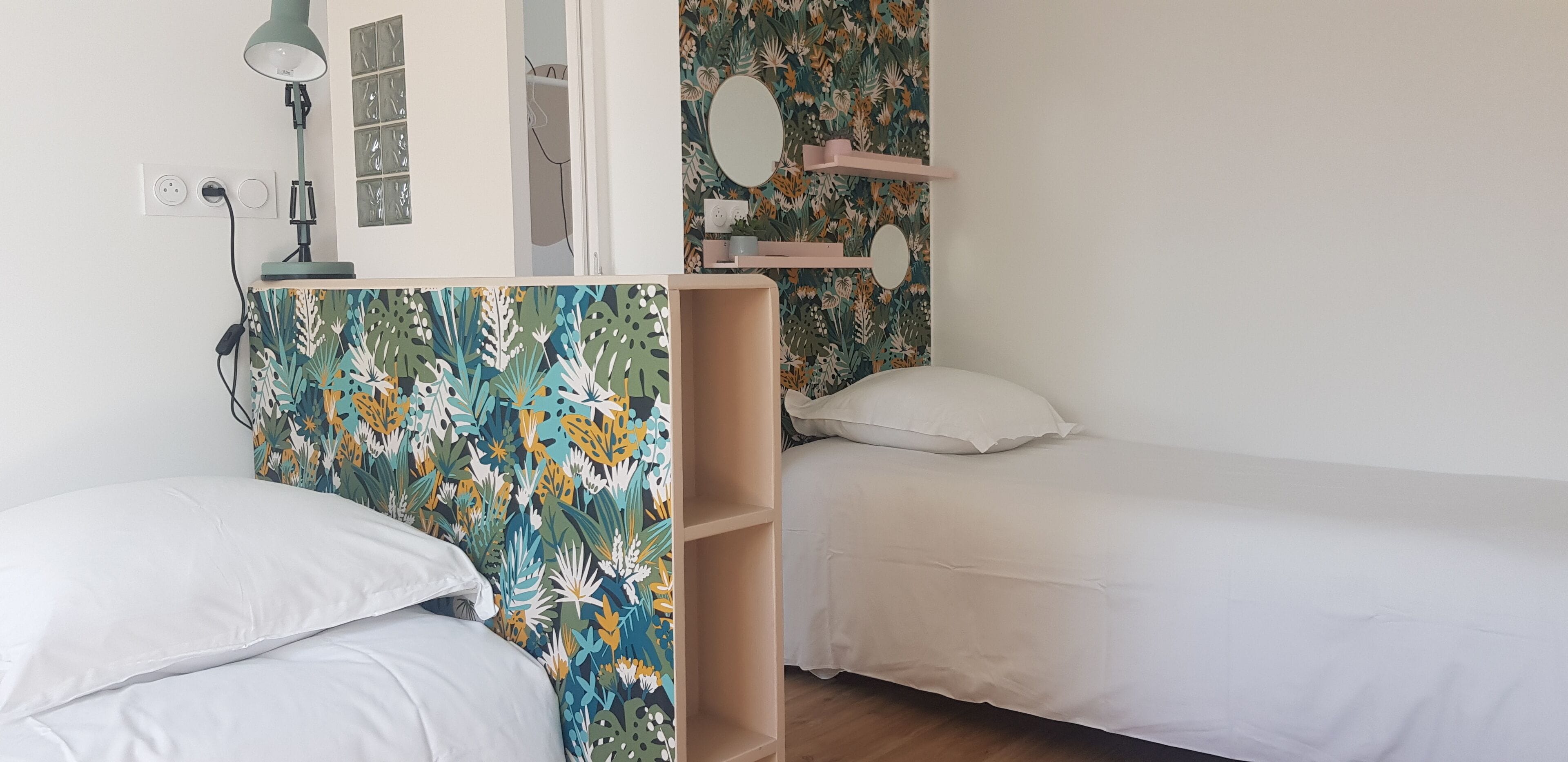 A bedroom with two single beds, a desk with a lamp, and a wall with a floral wallpaper.