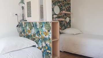 A bedroom with two single beds, a desk with a lamp, and a wall with a floral wallpaper.