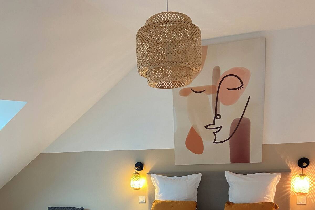 A bedroom with a large bed, two bedside lamps, a chair, and a hanging light fixture.
