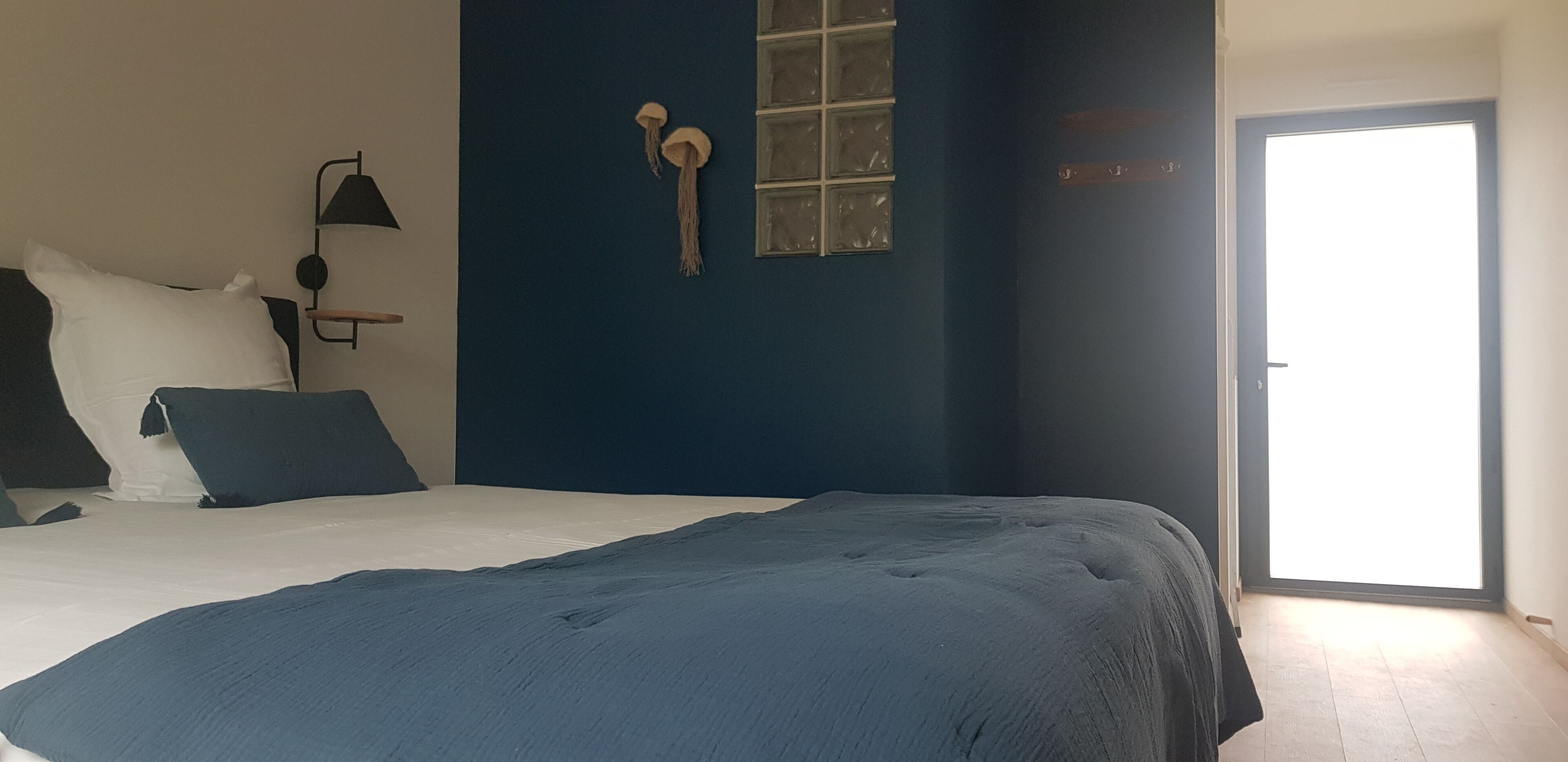 A bedroom with a bed, a nightstand, a wall-mounted lamp, a window, and a door.