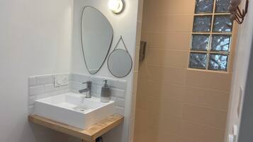 Un baño moderno con un lavabo blanco, un espejo y una zona de ducha con puerta de cristal.