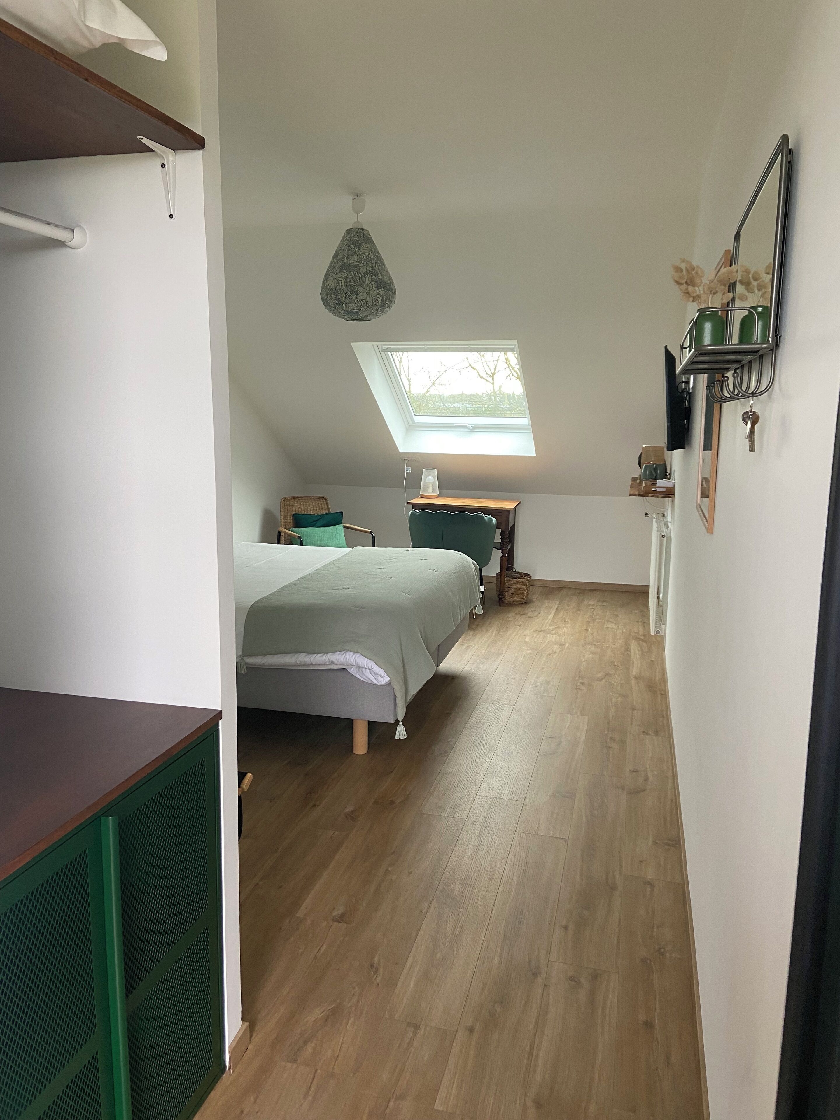 A small, cozy room with a sloped ceiling, a bed, a desk, and a skylight.